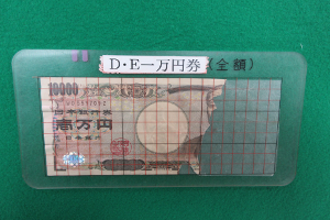 右側が破れているが残存面積が3分の2以上ある一万円札の上に、面積を確認するための鑑定版を乗せている様子