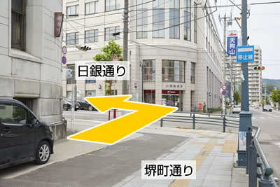 堺町通りと日銀通りの重なる交差点を撮影した写真で、郵便局が写っており、郵便局のある交差点において日銀通りを左折するように指示しています