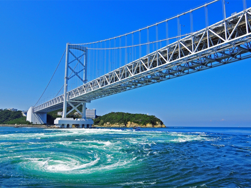 勇壮な鳴門海峡大橋と、その下で渦を巻く、鳴門の渦潮の風景の写真です。